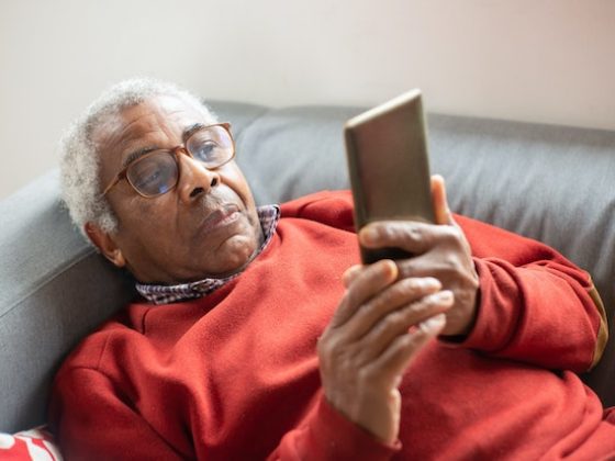 older man looking in the phone while laying down