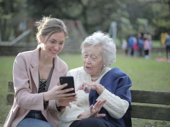 older and younger women sitting on a bench together and looking at a phone while smiling