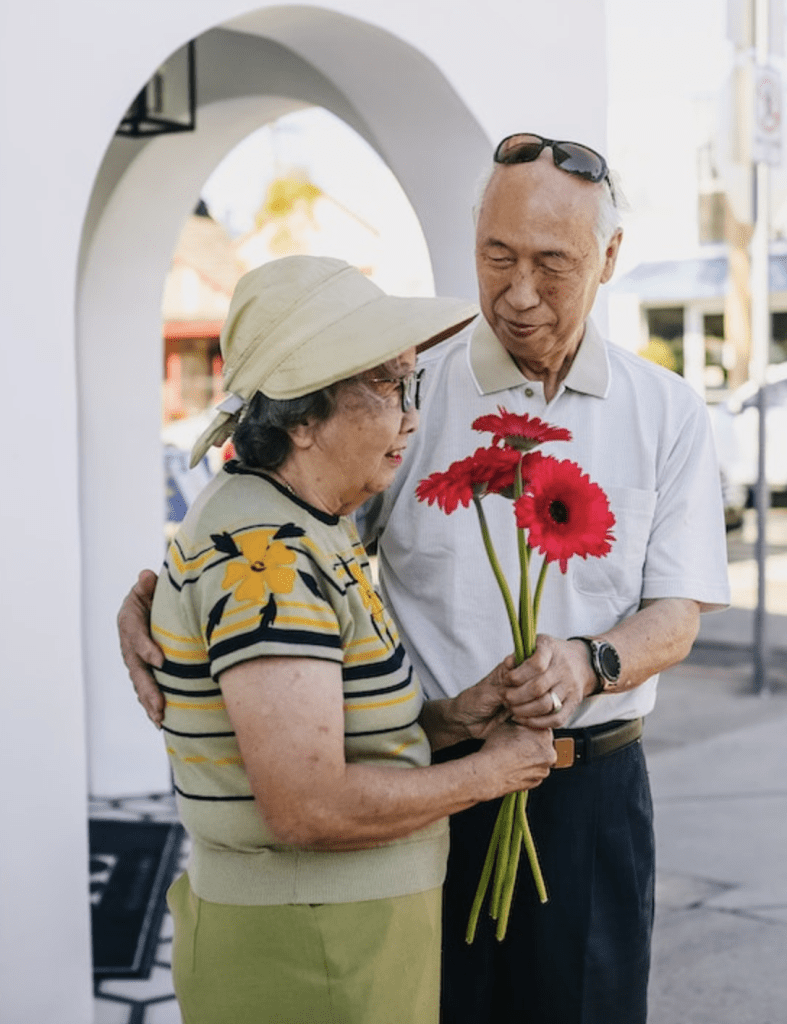 older couple standing outside, smiling and holding flowers